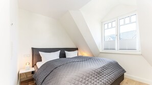 A bedroom with a bed, nightstand, and window. - This beautiful and new end terraced house is centrally located in Westerland (Westerland)