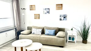 A living room with a sofa, two small tables, a radiator, a potted plant, and wall decorations. - Comfortable apartment with balcony, elevator and parking space in Westerland (Westerland)