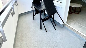 A balcony with two black chairs, a small table, and a window with blinds. - Comfortable apartment with balcony, elevator and parking space in Westerland (Westerland)