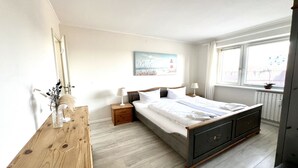 A bedroom with a bed, wooden nightstands, a dresser, a painting, and a window. - Comfortable apartment with balcony, elevator and parking space in Westerland (Westerland)