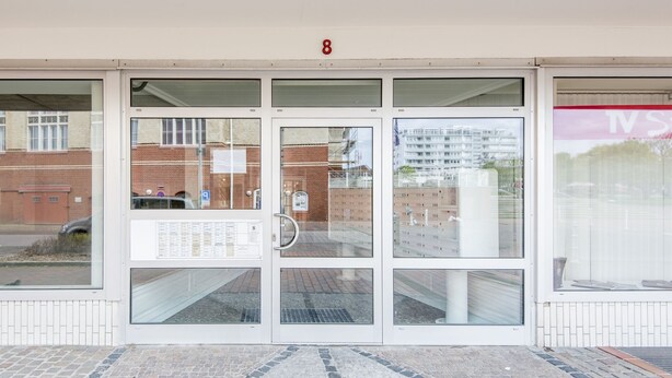 A building entrance with a glass door, a number '8' above, and a sign with text on the left. - Comfortable apartment with balcony, elevator and parking space in Westerland (Westerland)