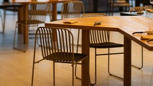 A modern dining area with wooden tables and metal chairs, large windows with a view of the city, and a clean, minimalist design. - Mentha Mare e Spa (Salerno)