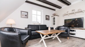 Ein modernes Wohnzimmer mit einer schwarzen Ledersofa, einem Holztisch und einem Fernseher auf einer weißen Kommode.