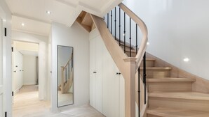 Eine moderne Treppe mit Holzbodenstufen und schwarzen Spindeln, die zu einem Ankleidebereich mit Spiegeln und weißen Türen führt.