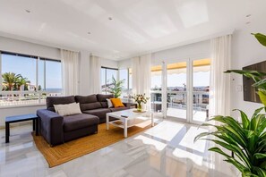 Ein modernes Wohnzimmer mit Sofa, Couchtisch und großen Fenstern mit Meerblick.