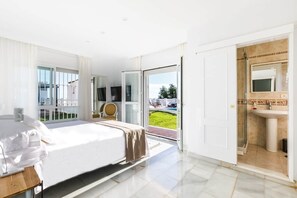 Ein modernes Hotelzimmer mit Bett, Fernseher, Badezimmer mit Waschbecken und Dusche sowie Blick ins Freie.