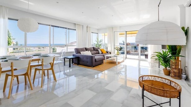 Un vaste espace de vie comprenant un canapé, une table à manger, des chaises et de grandes fenêtres donnant sur la mer.