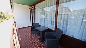 A balcony with a table and two chairs, a large window with curtains, and a brick floor. - Modern apartment in Westerland with balcony, parking and WiFi (Westerland)