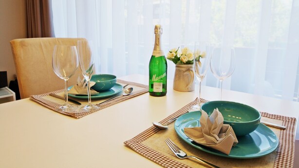A dining table set with green plates, wine glasses, and a bottle of champagne. - Modern apartment in Westerland with balcony, parking and WiFi (Westerland)