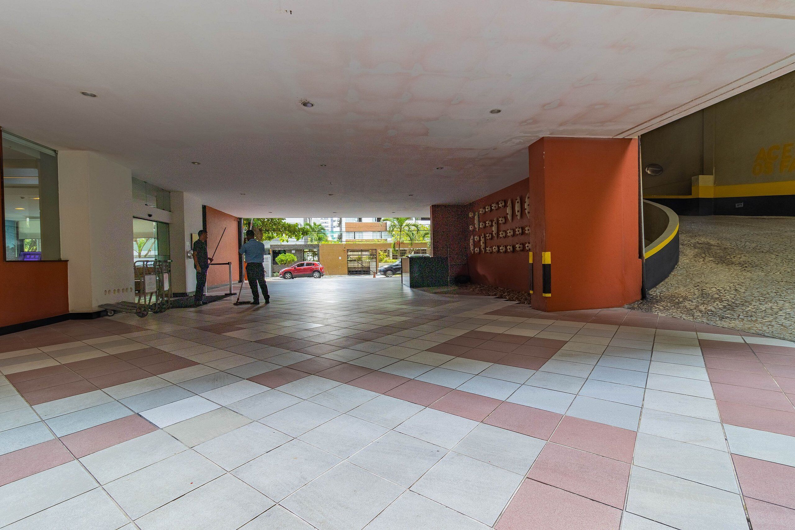 A spacious lobby with a tiled floor, a reception desk, and a visible car in the background.