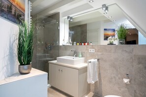 A modern bathroom with a glass shower enclosure, a sink with a mirror above, and a potted plant on the counter. - Beautiful and well-equipped vacation apartment in the south of Westerland. (Westerland)