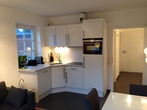 A compact kitchen with white cabinets, a built-in oven, and a window. - Modern apartment with sauna, terrace and garden in Wenningstedt (Wenningstedt)