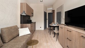Un espace de vie moderne comprenant un canapé, une petite table ronde, un téléviseur et un coin cuisine avec des placards et une machine à café.