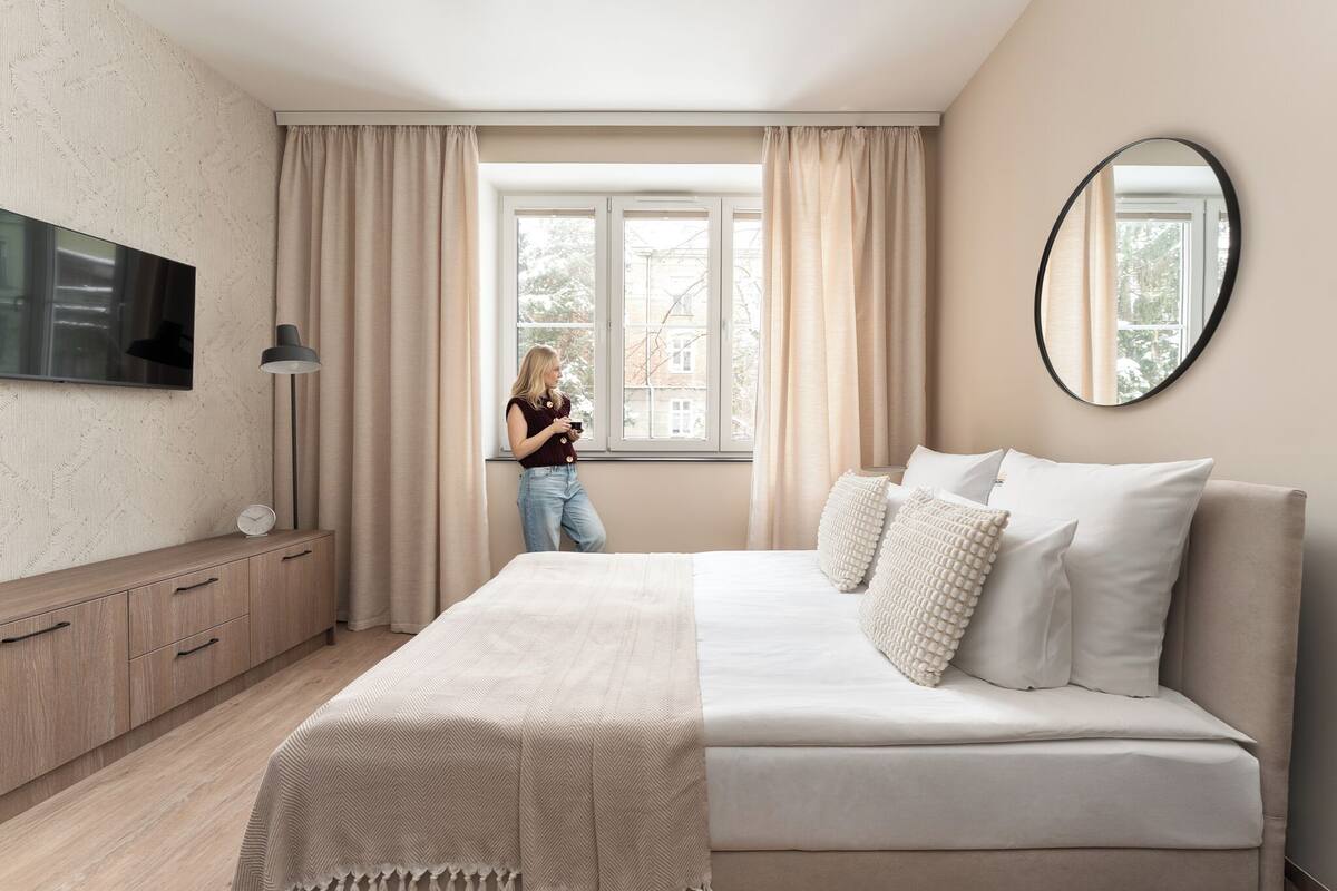 Un dormitorio con cama, televisor, cómoda y ventana con cortinas.