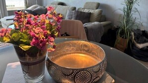 Ein modernes Wohnzimmer mit einer Couch, einem Couchtisch mit einer dekorativen Schale und Blumen, sowie einer Zimmerpflanze.