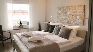 Ein modernes Schlafzimmer mit einem großen Bett, einem Schreibtisch und einem Fenster mit Blick auf Gebäude.