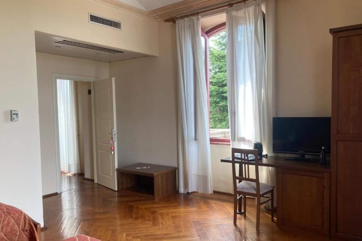 Una habitación con piso de madera, un televisor sobre un mueble, un escritorio con una silla y un armario.
