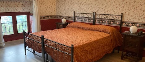 A bedroom with a bed, a nightstand, a wall-mounted lamp, a window with curtains, and a balcony view.
