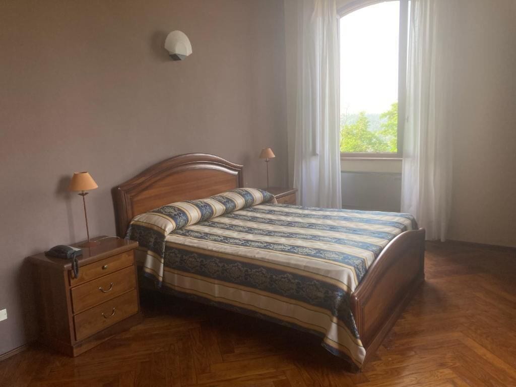 A bedroom with a wooden bed, two bedside lamps, a nightstand, and a window with curtains.