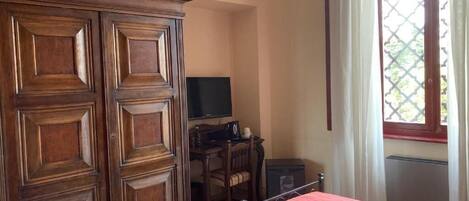 Un dormitorio con un amplio armario de madera, una cama con colcha estampada, un escritorio con televisor y una ventana con cortinas.