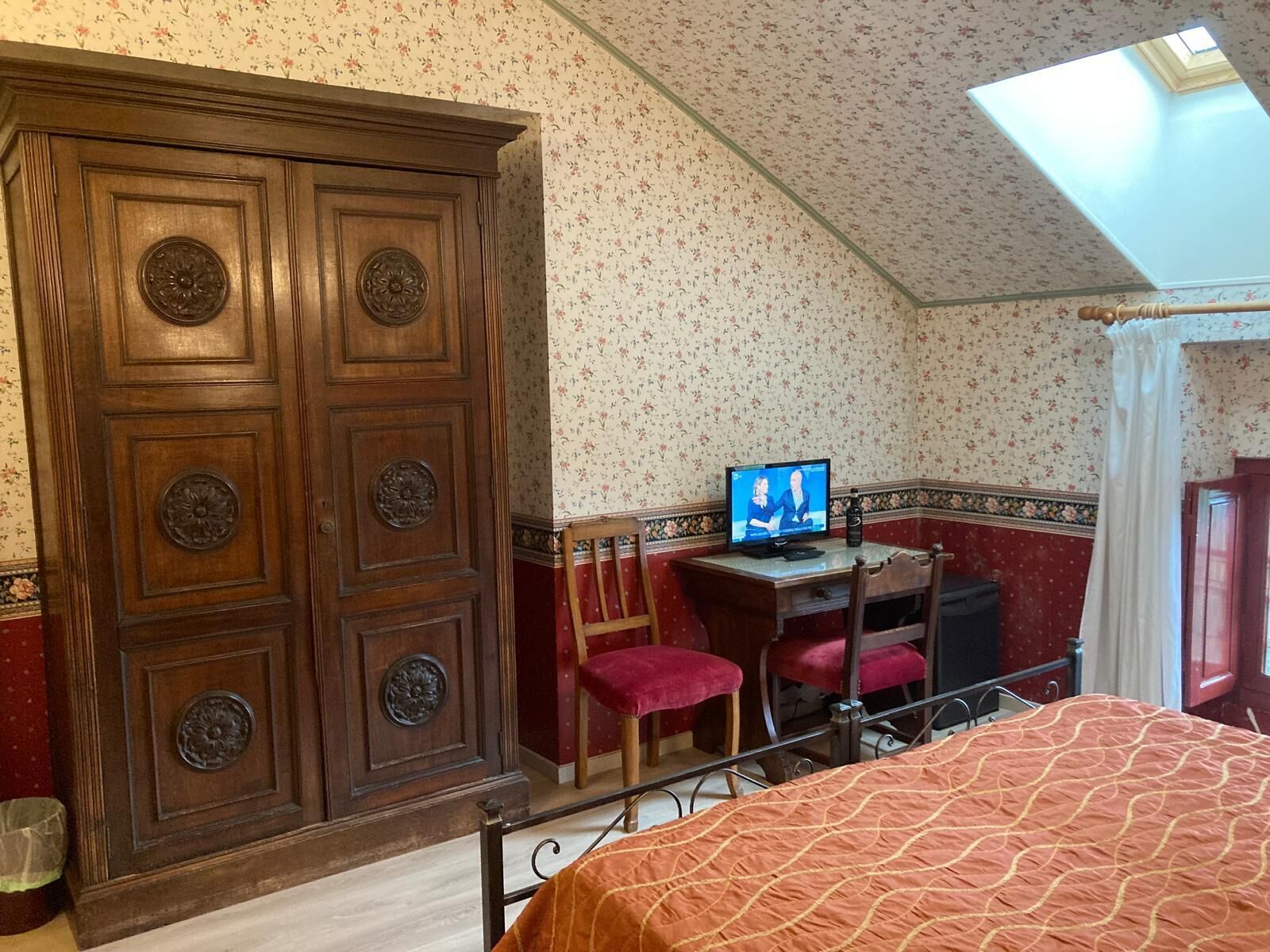 A bedroom with a wooden wardrobe, a desk with a computer, a bed, and a skylight.