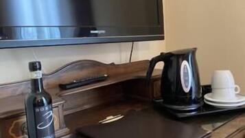 Un escritorio de madera con una computadora portátil, una botella, una cafetera y una taza.