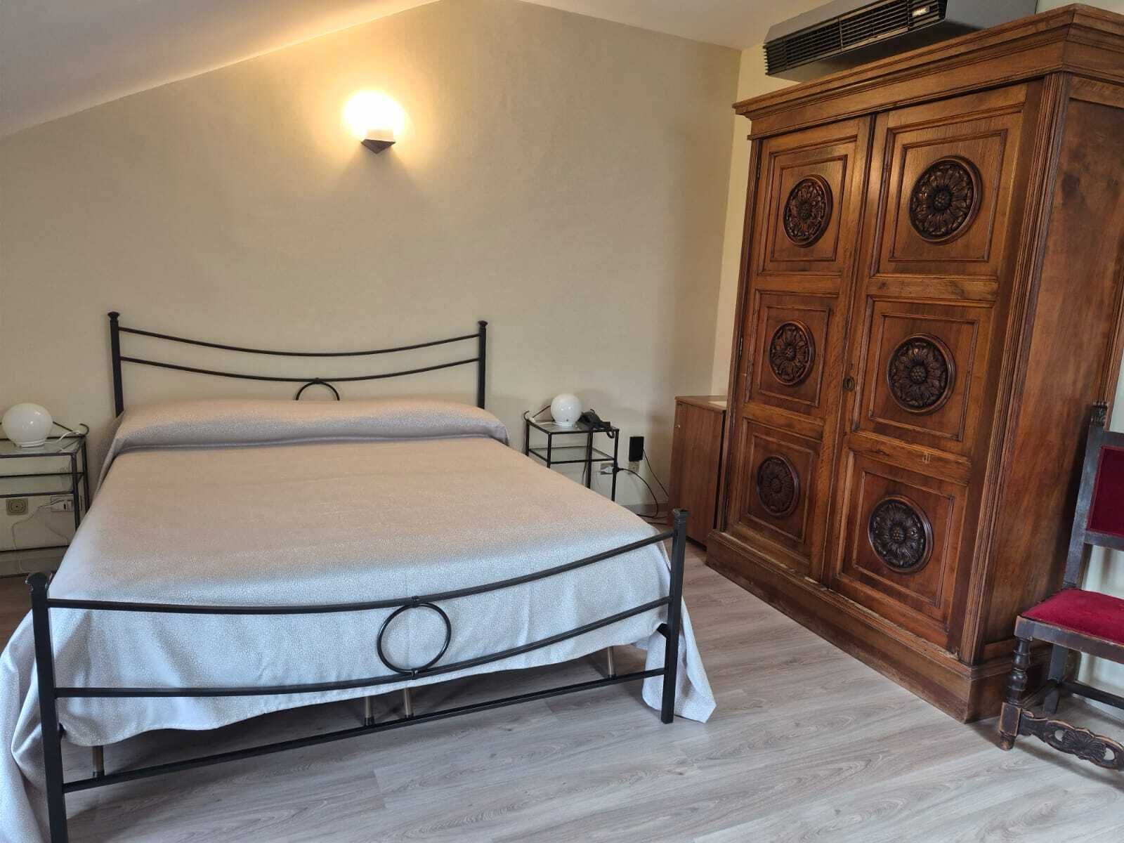 Un dormitori amb un llit, taules de nit, un armari i una làmpada penjada a la paret.