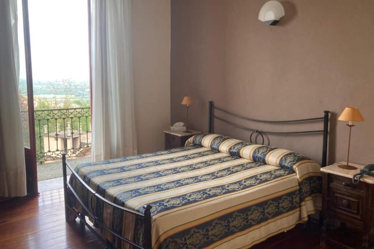 Un dormitorio con una cama, dos mesitas de noche, una lámpara y vistas al exterior.