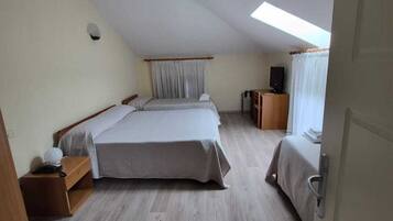 A room with a large bed, a desk, a chair, a television, and a skylight.