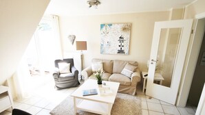 A living room with a sofa, armchair, coffee table, and a painting on the wall. - Cozy vacation apartment on the 1st floor in a quiet location in Wenningstedt (Wenningstedt)