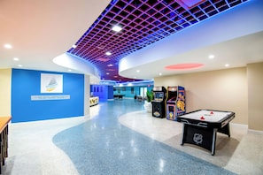 Un hall d’entrée spacieux avec un plafond incurvé, une table de baby-foot et un mur bleu orné d’un logo.