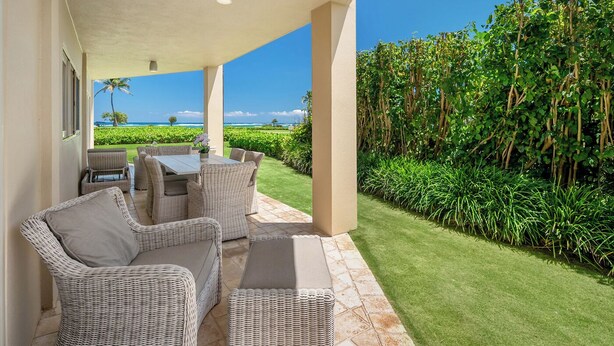 Um pátio externo com móveis de vime, uma mesa e vista para o oceano.