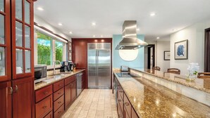 Uma cozinha moderna com armários de madeira, eletrodomésticos de aço inoxidável, bancada de granito e vista para o exterior.