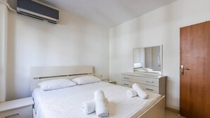 Ein sauberes, modernes Hotelzimmer mit Bett, Nachttisch, Kommode, Spiegel und Holztür.