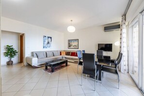 Een moderne woonkamer met een bank, salontafel en stoelen. Er is een televisie en een schilderij aan de muur.