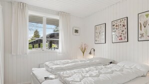 Una camera da letto con due letti, una finestra con tende e stampe botaniche incorniciate al muro.
