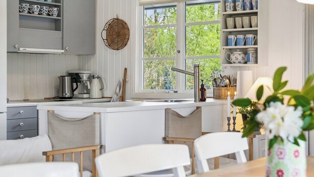 Cucina con mobili bianchi, una macchina da caffè e una finestra vista sul verde.