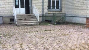 Un edificio con fachada de ladrillo, una escalera que lleva a una puerta y un patio empedrado.