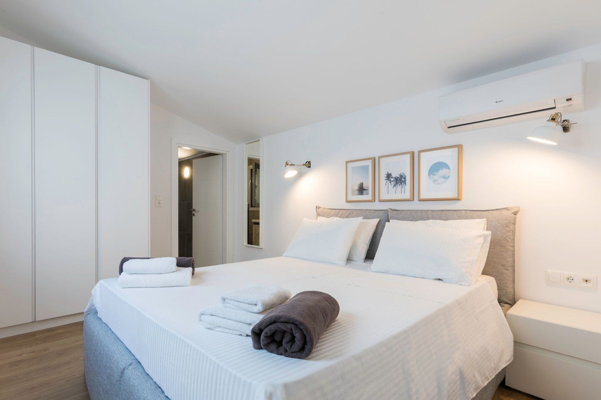 Een moderne slaapkamer met een groot bed, witte lakens, een nachtkastje en een kledingkast.