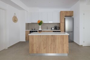 A modern kitchen with white cabinetry, a wooden island, and a stainless steel refrigerator. - Splendid Rhodes Villa | Villa Ialysos | 4 Bedrooms | Breathtaking Sea Views |. (Lindos)