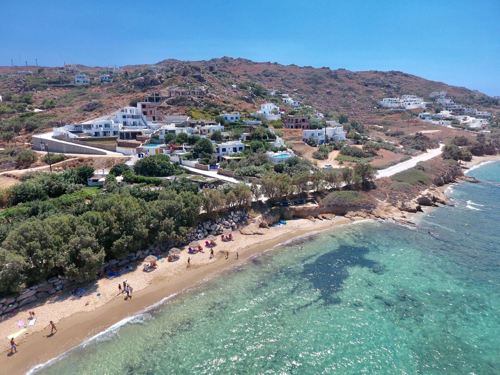 Un resort costero con edificios blancos, una playa de arena y aguas azul cristalino.