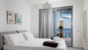 Una moderna camera d'hotel con un ampio letto, vista sul mare tramite una porta scorrevole in vetro e due quadri appesi al muro.