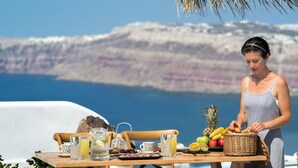 Ein Tisch, gedeckt mit Frühstücksleckereien, ein Korbwesen und ein malerischer Blick auf eine Küstenlandschaft.