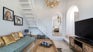 Ein geräumiges Wohnzimmer mit Treppe, einem großen Fernseher und einer Couch mit dekorativen Kissen.