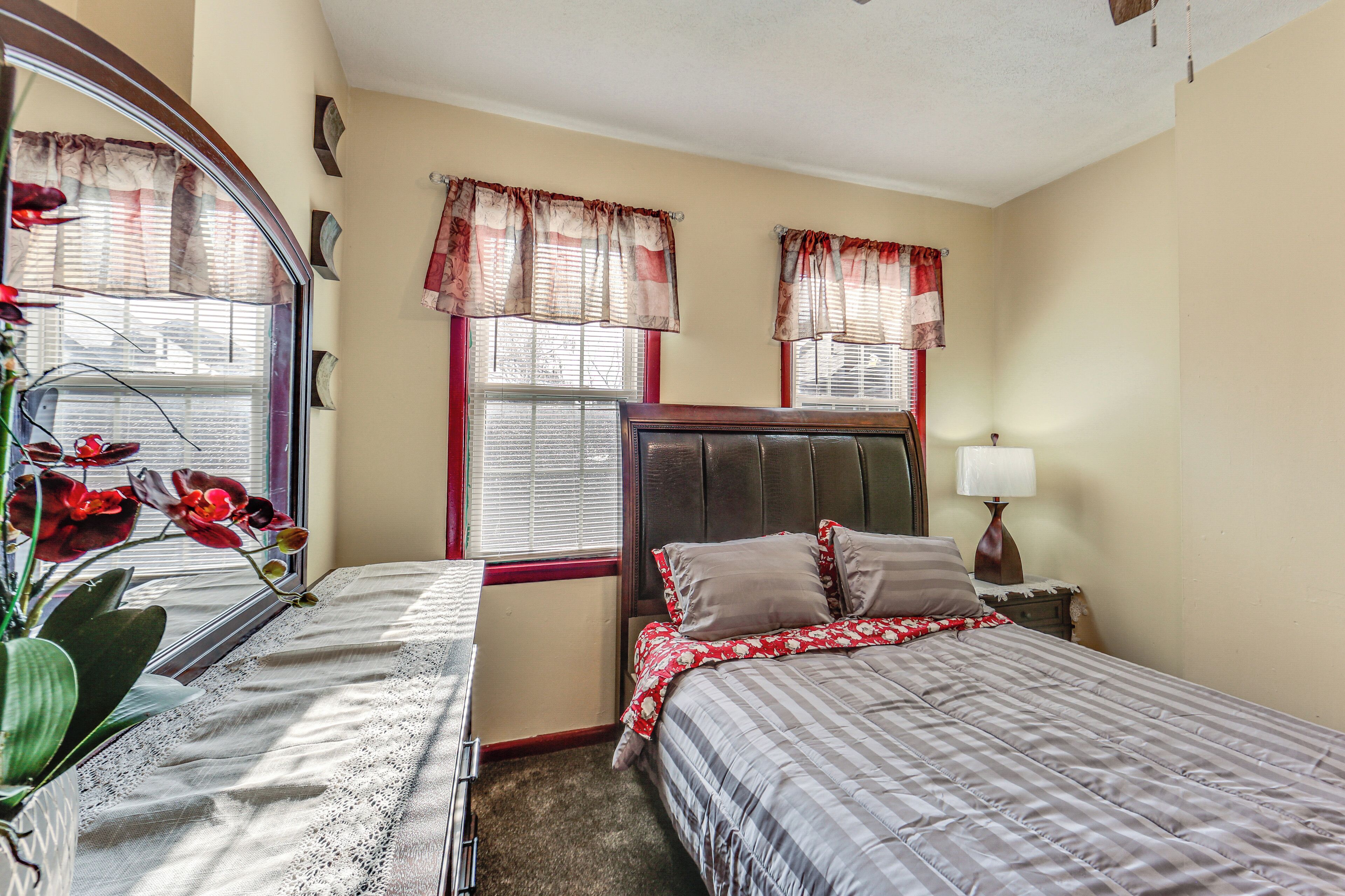 A bedroom with two beds, a large mirror, a nightstand with a lamp, and a window with curtains.