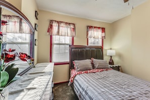 A bedroom with two beds, a large mirror, a nightstand with a lamp, and a window with curtains.