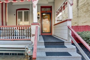A building entrance with a red and white porch, a set of steps leading to a door, and a small outdoor area with a bench.