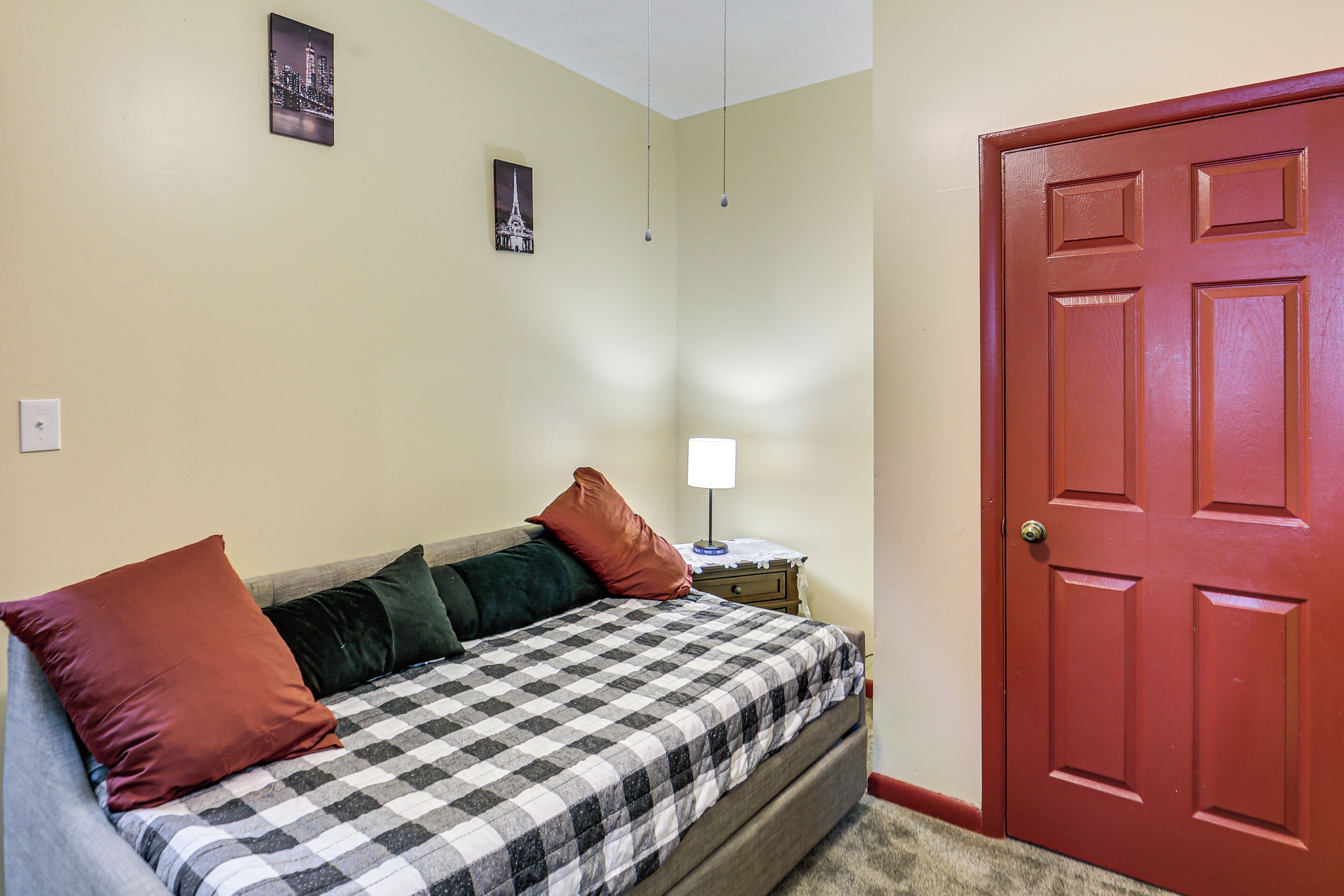 A bedroom with a bed, pillows, a nightstand, a lamp, and a door.