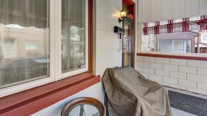 Un porche cubierto con una ventana, una luz de pared y una puerta con un toldo rojo.