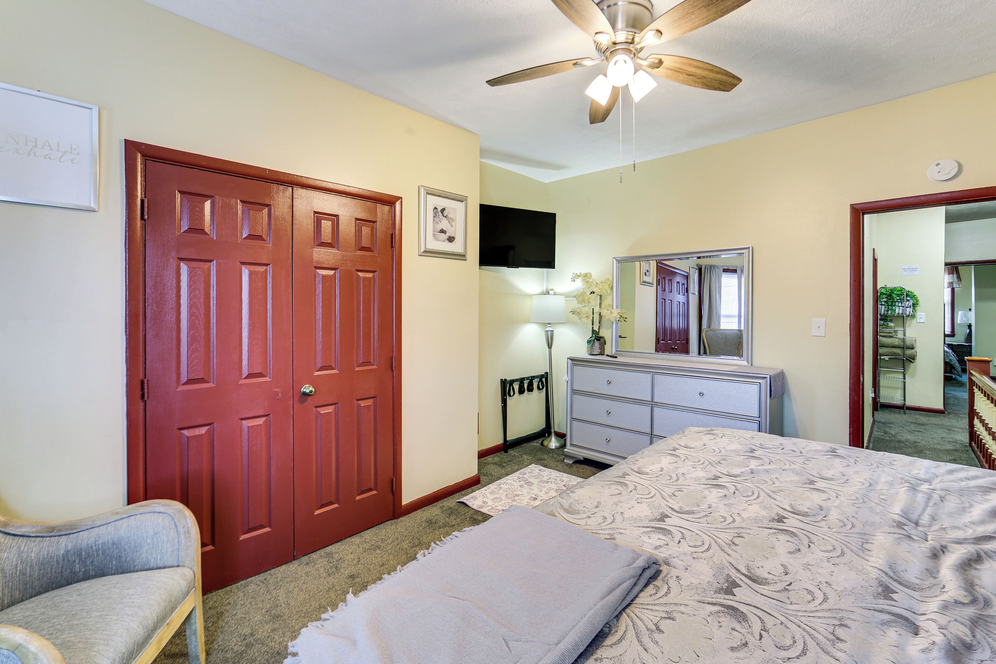 A bedroom with a bed, a dresser, a chair, a ceiling fan, and a door.